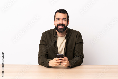 Caucasian man with beard in a table sending a message with the mobile.