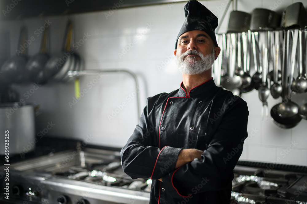 Mature chef in black coat with folded arms in his kitchen Mature chef in black coat with folded arms in his kitchen