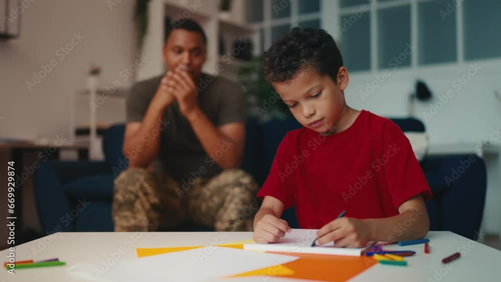 Man in military uniform looking at little son drawing picture, family time Man in military uniform looking at little son drawing picture, family time