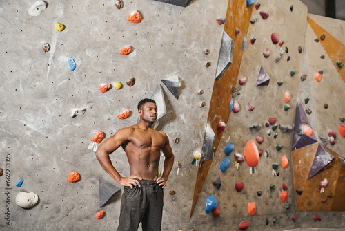 handsome muscular african american man posing topless next to climbing wall with his arms akimbo