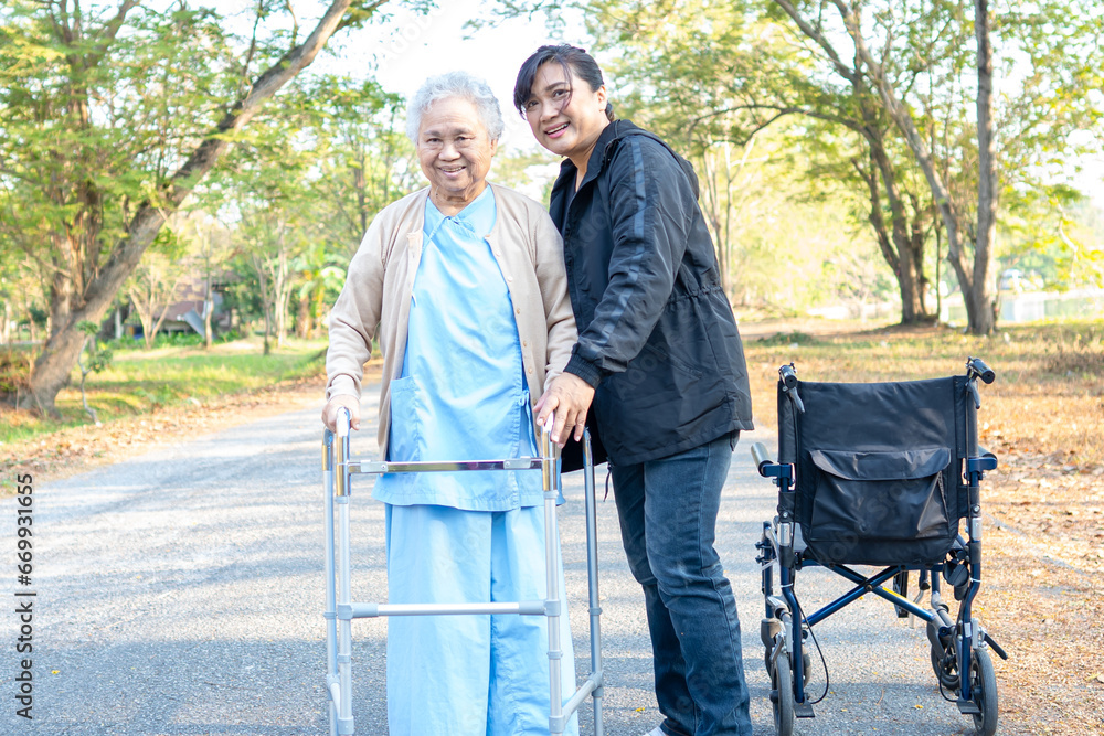 Caregiver help Asian senior woman walk with walker with wheelchair at park. Caregiver help Asian senior woman walk with walker with wheelchair at park.