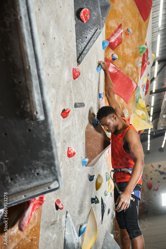 vertical shot of african american man hanging on his fingers on rock wall and looking down