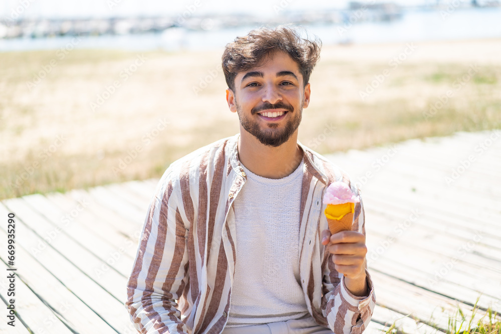 Handsome Arab man with a cornet ice cream at outdoors smiling a lot - obrazy, fototapety, plakaty 