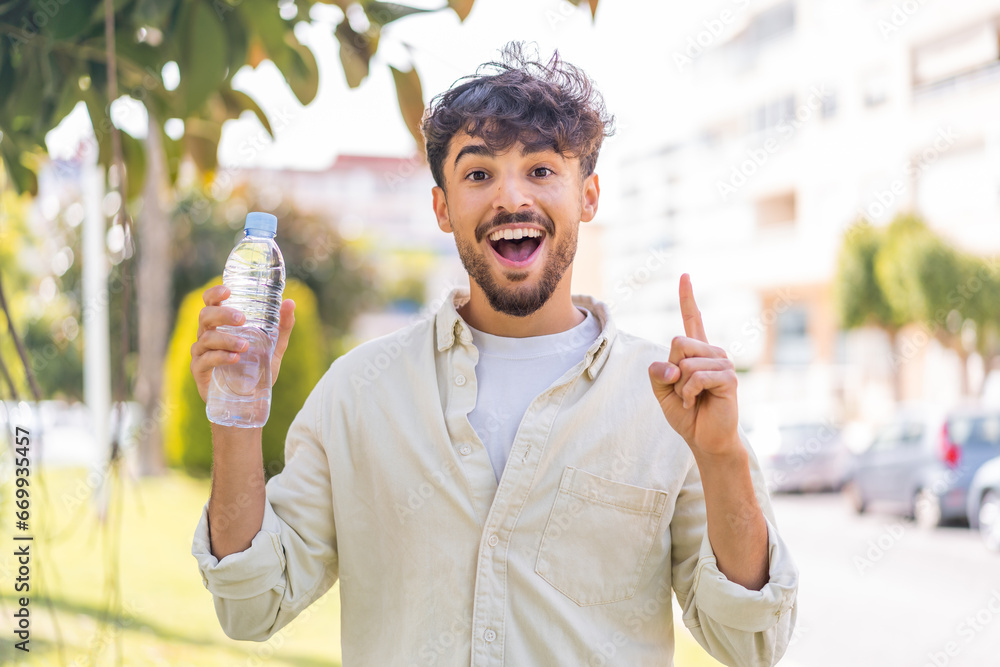 © luismolinero - Young Arabian handsome man with a bottle of water at outdoors pointing up a great idea © luismolinero - Young Arabian handsome man with a bottle of water at outdoors pointing up a great idea