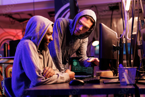 Hackers smiling while cracking encrypted information successfully on computer and working together in hideout place. Two criminals coding illegal malicious software for server hacking © DC Studio