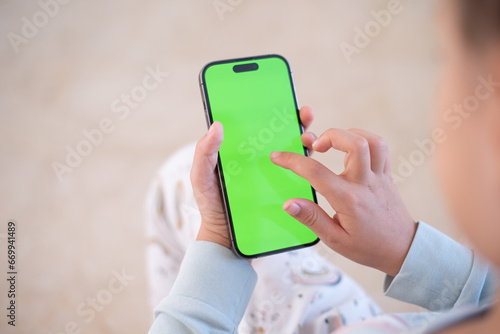 Children’s hands hold phone with green screen. Kid hold phone by two hands. Light background.