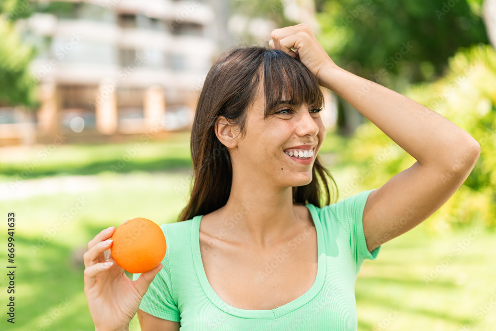 Young woman holding an orange at outdoors has realized something and intending the solution Young woman holding an orange at outdoors has realized something and intending the solution