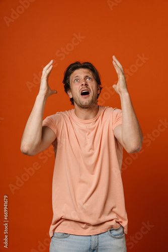 Displeased man screaming and gesturing while standing isolated over red wall
