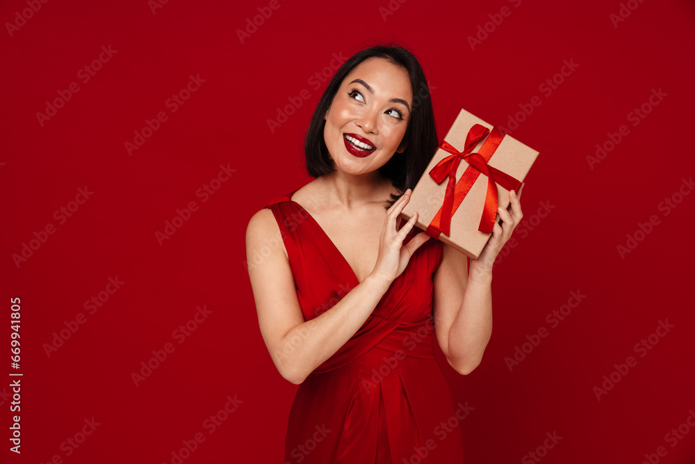 Smiling woman holding gift box while standing isolated over red background Smiling woman holding gift box while standing isolated over red background