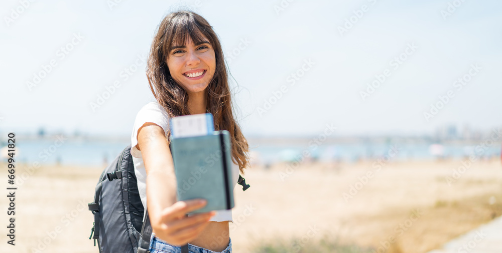 Young woman at outdoors holding a passport with happy expression