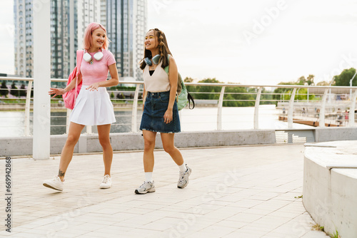 Two cheerful teen girls walking together in city park