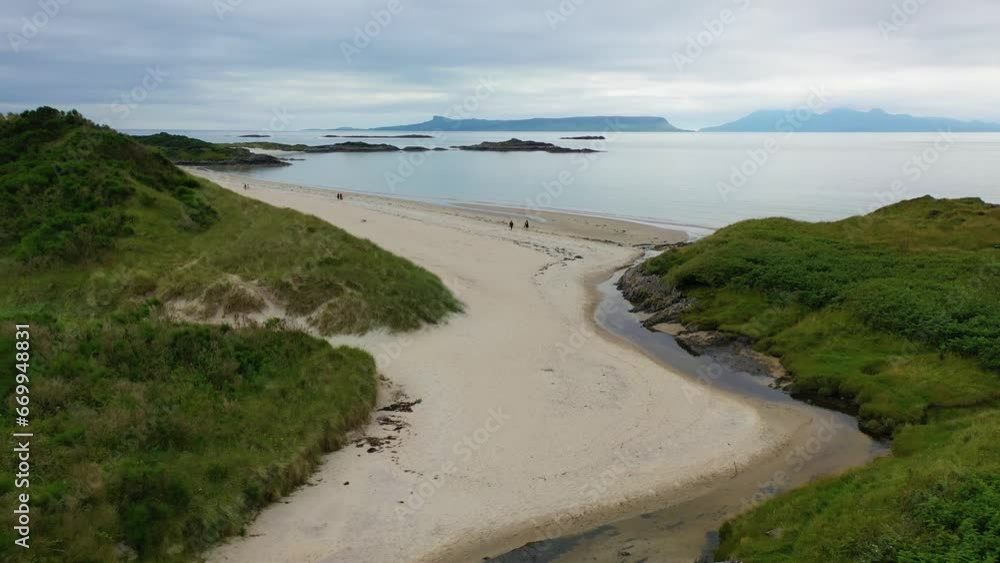 Drone shot featuring couples walking on Scottish beach Camusdarach near Morar on the West Coast of Scotland, United Kingdom. Isle of Eigg and Rum in the distance. Drone shot featuring couples walking on Scottish beach Camusdarach near Morar on the West Coast of Scotland, United Kingdom. Isle of Eigg and Rum in the distance.