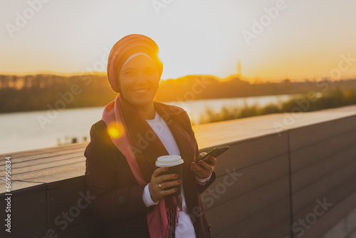 Modern arab woman in hijab walking by street and drinking coffee take away in spring time morning, copy space