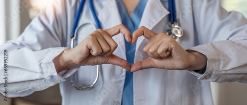 close up, Beautiful asian woman wearing doctor uniform and stethoscope smiling in love doing heart symbol shape with hands. romantic concept. photo
