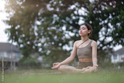 Young Asian woman doing yoga, meditation on a calm yoga mat in a green park in the early morning. Young woman wearing brown yoga clothes Yoga concept
