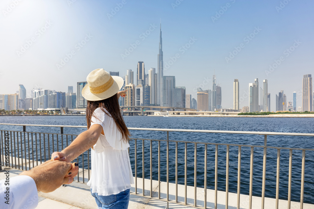 Concept of Dubai travel and tourism with a tourist woman pulling her partners hand towards the urban skyline of the city, UAE