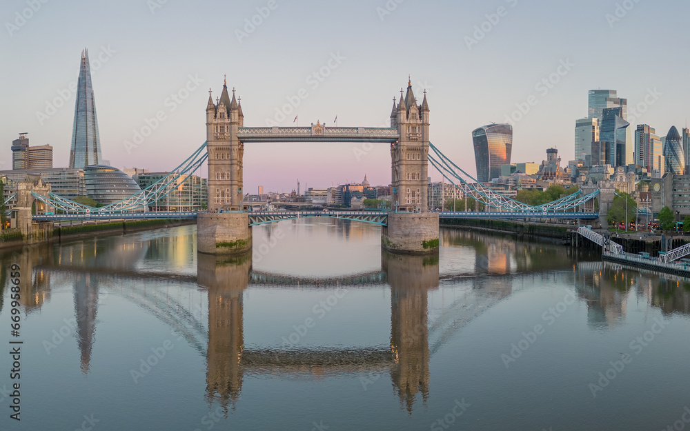 Tower Bridge, London England,  reflected in the River Thames at sunrise with the city of London in the background including landmark buildings of the financial district