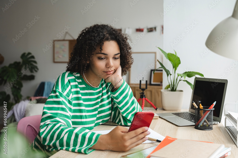Smiling teenage girl using smart phone at desk in bedroom Smiling teenage girl using smart phone at desk in bedroom