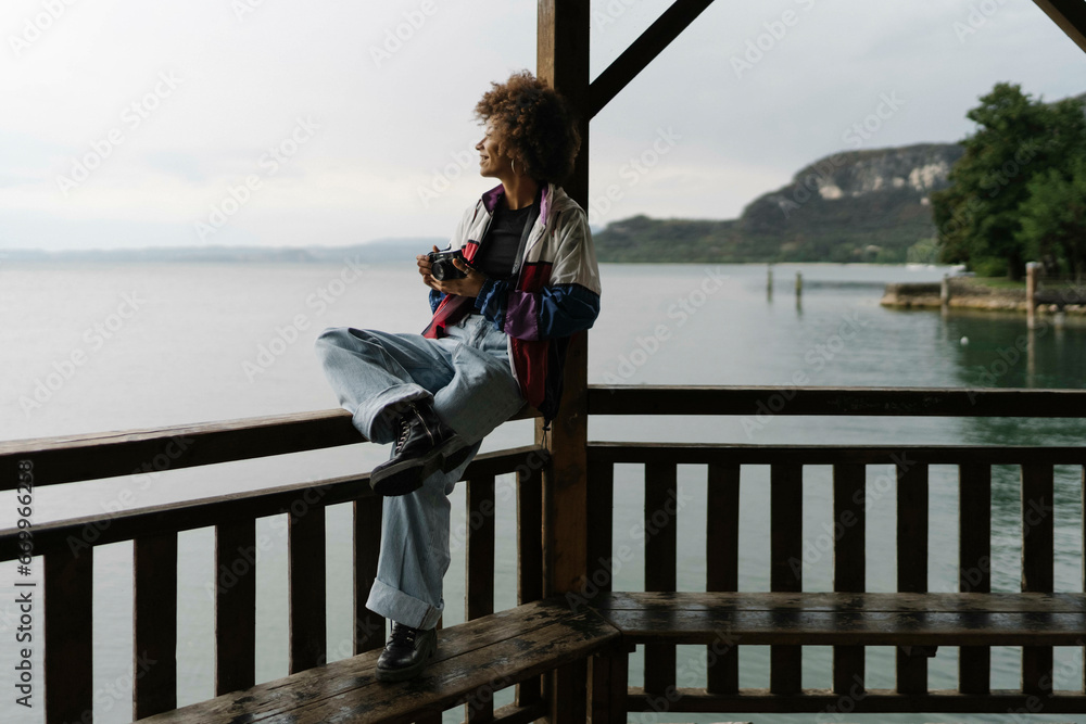 Thoughtful young woman sitting on railing in front of lake Thoughtful young woman sitting on railing in front of lake