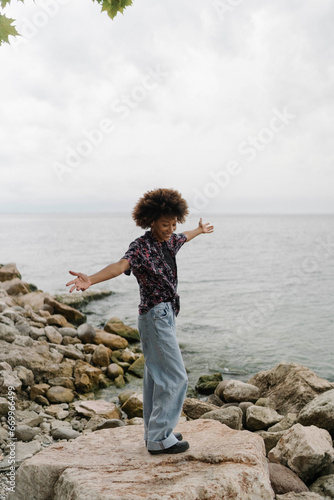 Carefree young woman with arms outstretched standing near lake