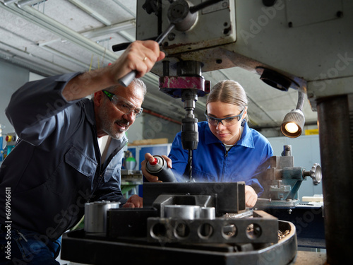 Trainee spraying lubricant on drill bit with instructor at workshop