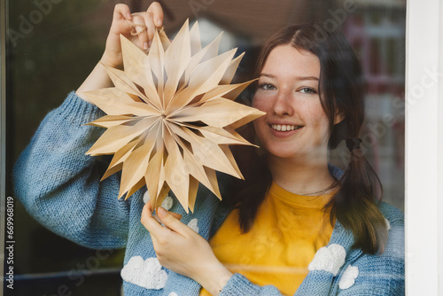 Smiling girl holding star shaped Christmas decoration seen through glass photo