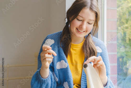 Smiling teenage girl sewing button on clothing photo