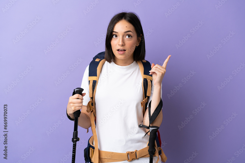 Young caucasian woman with backpack and trekking poles isolated on blue background thinking an idea pointing the finger up