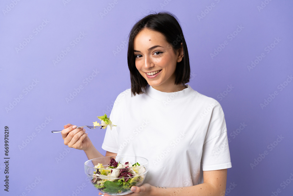 Young caucasian woman isolated on purple background holding a bowl of salad with happy expression Young caucasian woman isolated on purple background holding a bowl of salad with happy expression