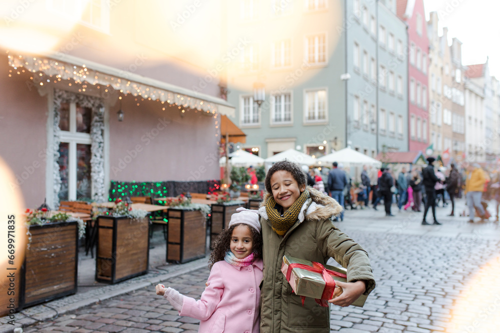Smiling brother holding gift box and standing with brother at Christmas market Smiling brother holding gift box and standing with brother at Christmas market