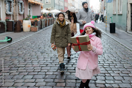 Happy girl holding gift box and walking with family at Christmas market photo