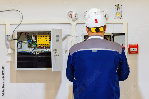 Electrician near power cabinet. Male electrical equipment repairman. Electrician guy with his back to camera. Electrician repairs power panel. Worker from energy company. Setting up electricity photo