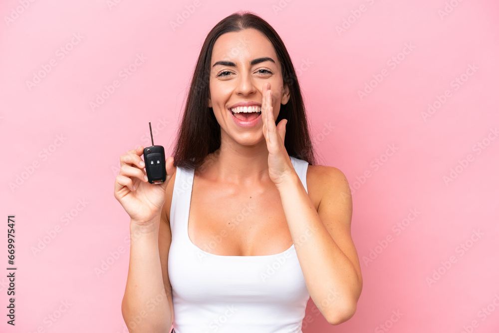 Young caucasian woman holding car keys isolated on pink background shouting with mouth wide open Young caucasian woman holding car keys isolated on pink background shouting with mouth wide open