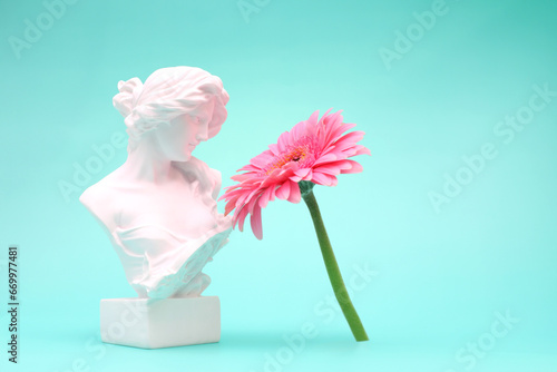 Female bust sculpure greek style with gerbera flower on blue background