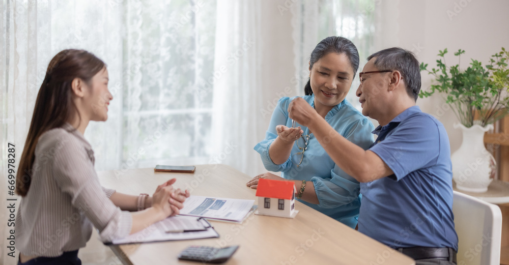 Elderly couples satisfying retirement home purchase with contract and key handover from a saleswoman Elderly couples satisfying retirement home purchase with contract and key handover from a saleswoman