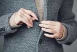 Close-up of a gray knitted jacket. Women's hands fasten buttons. Winter, autumn warm woolen clothes.