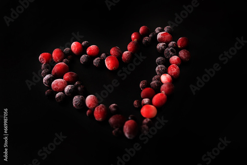 frozen cranberries and black currants on a black background in the shape of a heart