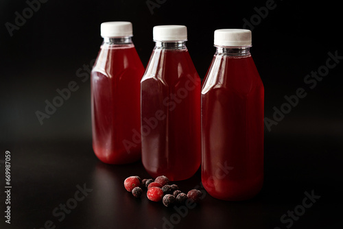 three plastic bottles with cranberry and currant juice and frozen berries on a black background