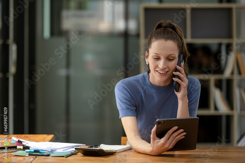 Businesswoman talking on the phone with friend or colleague while checking documents in modern office