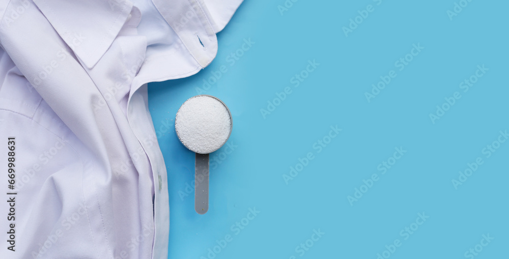 Detergent powder in measuring spoon with cloth before washing. Laundry concept. - obrazy, fototapety, plakaty 