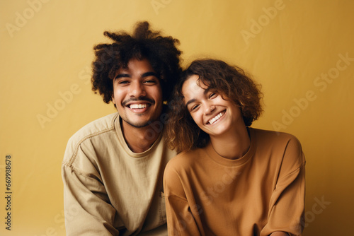 Middle shot of a couple of friends smiling and looking at the camera in a brown studio background © alisaaa