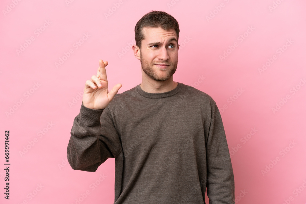 Young caucasian man isolated on pink background with fingers crossing and wishing the best Young caucasian man isolated on pink background with fingers crossing and wishing the best