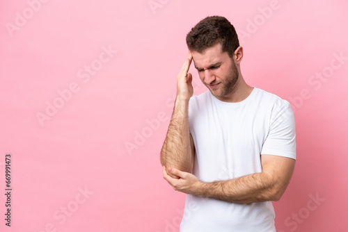 Young caucasian man isolated on pink background with headache