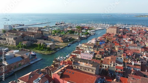Aerial flight over the old port city of Chioggia with red roofs, narrow streets and lots of canals.