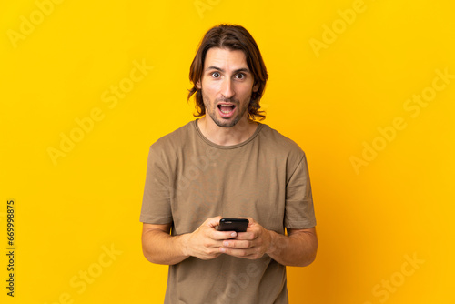 Young handsome man isolated on yellow background surprised and sending a message