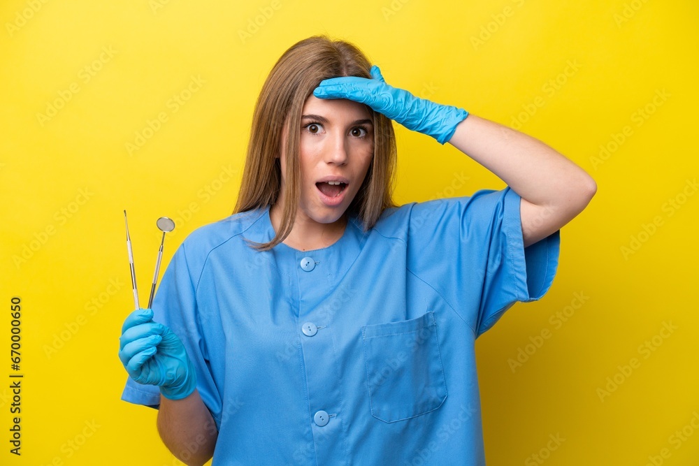 Dentist caucasian woman holding tools isolated on yellow background doing surprise gesture while looking to the side Dentist caucasian woman holding tools isolated on yellow background doing surprise gesture while looking to the side