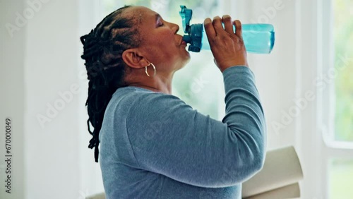 Senior woman, drinking water and bottle with yoga mat for hydration, energy and wellness in home. Elderly African lady, training and exercise for health with detox, nutrition and diet in house photo