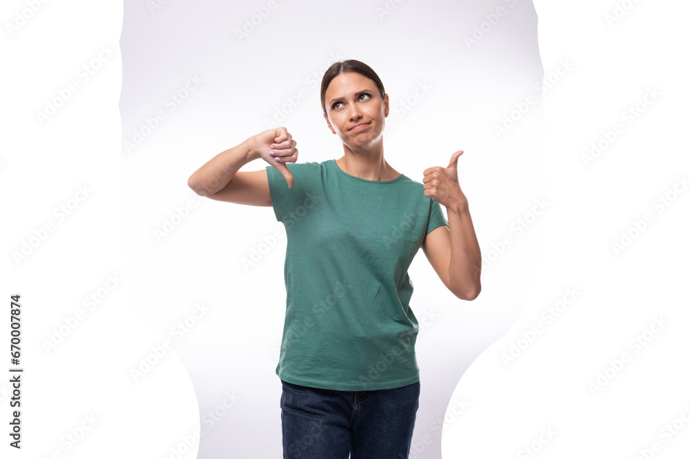 young dreamy beautiful brunette lady with ponytail hairstyle dressed in green t-shirt and jeans holding thumbs up young dreamy beautiful brunette lady with ponytail hairstyle dressed in green t-shirt and jeans holding thumbs up