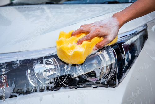 Woman hand with yellow sponge washing headlight modern car or cleaning automobile. Car wash concept