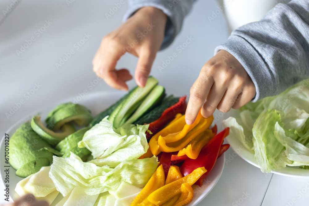 Hands and a plate with chopped vegetables on the kitchen table. Hands and a plate with chopped vegetables on the kitchen table.